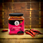 Jar of chicken pickle with a pink label on a wooden surface with red peppers.
